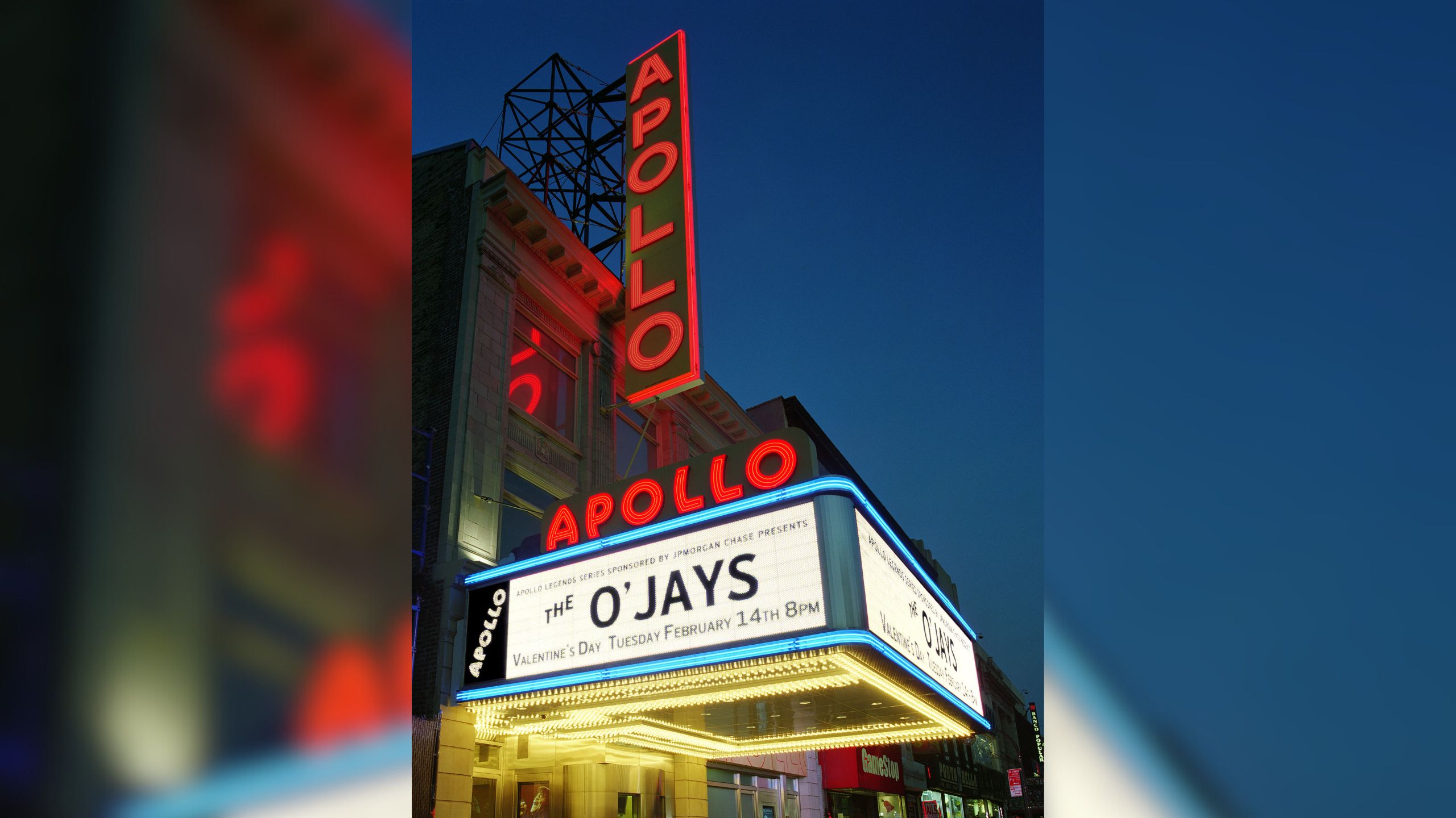 The exterior of the Apollo Theater at dusk, showing its neon blade sign and marquee with the theater name in red.